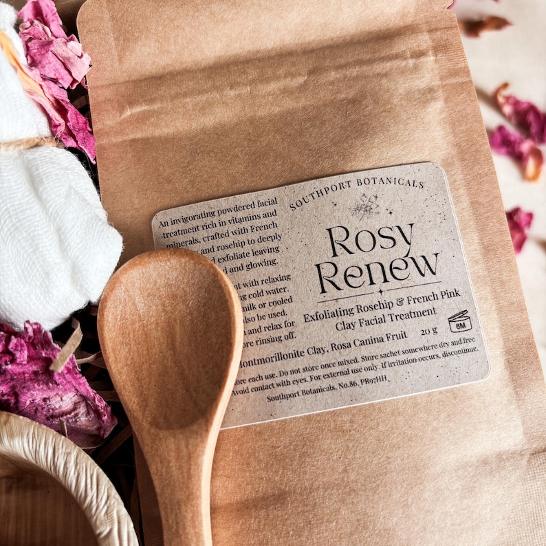 K&ouml;nnte beinhalten: Ein brauner Papierbeutel mit Southport Botanicals Rosy Renew Peeling-Gesichtsbehandlung aus Hagebutte und franz&ouml;sischer rosa Tonerde, 20 g, dazu ein Holzl&ouml;ffel, ein wei&szlig;es Tuch und getrocknete rosa Bl&uuml;tenbl&auml;tter. Das Etikett enth&auml;lt Anweisungen.