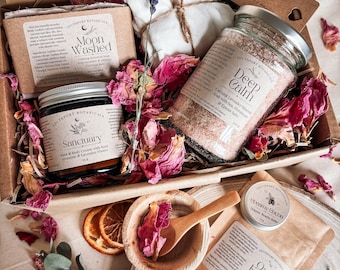 May include: A gift box containing a bar of Moon Washed soap, a jar of Deep Calm mineral soak, a jar of Sanctuary hand and body cream, a small tin of Creamy Cocoa balm, a bag of Oat and Ember facial treatment, a wooden bowl with a spoon, and dried flowers.