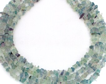 May include: A necklace made of multiple strands of small, irregularly shaped, light green, blue, and purple fluorite stones. The necklace is displayed against a white background.