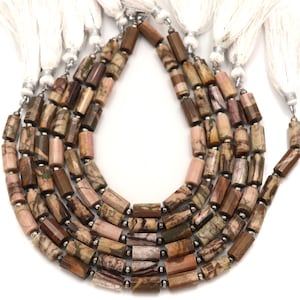 Puede incluir: Un collar de múltiples hilos con cuentas cilíndricas en tonos marrón, rosa y crema con vetas naturales. Los hilos están separados por pequeñas cuentas espaciadoras metálicas y terminados con borlas de tela blanca en cada extremo.