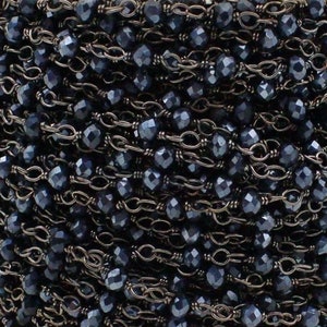 Peut inclure: Gros plan d'une bobine de chaîne de perles bleu foncé. La chaîne est composée de petites perles à facettes enfilées avec une chaîne en métal foncé. Les perles ont une qualité réfléchissante, et la chaîne est enroulée serrée.
