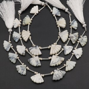 Peut inclure: Colliers de pierres précieuses blanches et grises en forme d'éventail. Les perles sont enfilées avec du métal argenté et de petites perles blanches. Des pompons blancs ornent le haut de chaque collier.