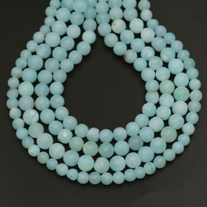 Puede incluir: Cadenas de cuentas redondas de piedras preciosas de color azul claro. Las cuentas, de diferentes tamaños, están ensartadas, creando un diseño de collar o pulsera. Las cuentas tienen una superficie lisa y pulida, con una sutil variación natural de color.