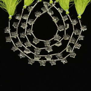 May include: Strands of clear, star-shaped beads strung on silver wire. Each strand is finished with a bright green tassel. The beads are faceted, catching the light. The background is solid black.