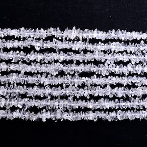 Op de afbeelding: Close-up van meerdere strengen heldere kwarts chip kralen tegen een zwarte achtergrond. De kralen hebben verschillende maten en vormen en zijn geregen. Het kwarts is doorschijnend en creëert een textuur.
