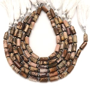 May include: Strands of gemstone beads in shades of brown, pink, and green. The beads are cylindrical with a polished finish and are strung together with silver-colored findings. White tassels are attached to the top of each strand. The beads are likely used for jewelry making.