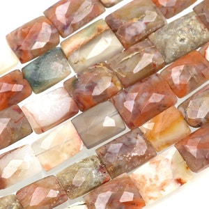 Puede incluir: Primer plano de una colección de cuentas rectangulares de piedras preciosas. Las cuentas tienen una superficie facetada y muestran una mezcla de colores, incluyendo tonos de naranja, marrón, gris y blanco. Las cuentas están dispuestas juntas, mostrando sus patrones únicos.