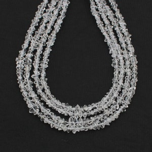 Puede incluir: Una hebra de cuentas de cristal de cuarzo transparente, con un acabado facetado y de corte tosco. Las cuentas están enhebradas en un hilo transparente y están dispuestas en un patrón suelto y fluido.