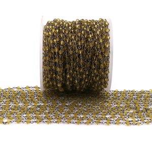 May include: A spool of gold-toned glass beads strung on a silver chain. The beads are small and round, and the chain is delicate.