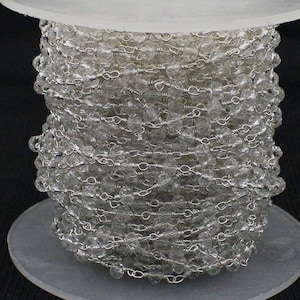 May include: A clear crystal bead chain wound on a spool. The beads are faceted and linked with silver-coloured wire. The chain is on a white and clear plastic spool. Ideal for jewellery making or craft projects. The beads are clear and catch the light.