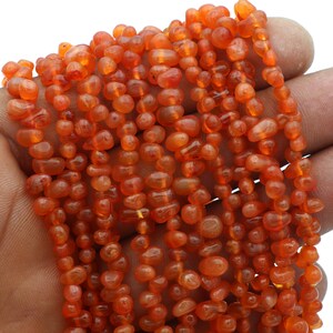 Op de afbeelding: Een streng oranje carneol kralen, elke kraal heeft een gladde, onregelmatige vorm. De kralen zijn geregen op een doorzichtige draad.