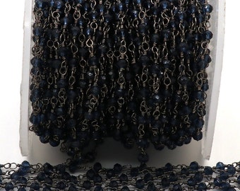May include: A close-up of a dark blue gemstone chain with silver links. The chain is wound around a clear plastic spool.