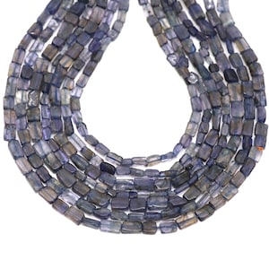Puede incluir: Hebras de cuentas rectangulares de piedra preciosa azul-gris. Las cuentas translúcidas están ensartadas, formando un collar o componente de joyería. Las cuentas muestran una mezcla de tonos claros y oscuros de azul y gris.