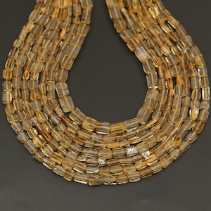 May include: A strand of golden citrine beads, each bead is faceted and rectangular in shape. The beads are strung together to form a long necklace.