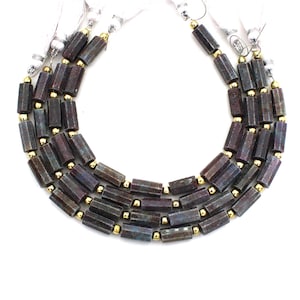 Op de afbeelding: Een streng donkergrijze en paarse edelsteen kralen met gouden accenten. De kralen zijn gefacetteerd en hebben een zeshoekige vorm. De kralen zijn geregen op een koord en zijn klaar om tot sieraden te worden verwerkt.