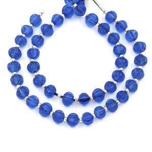 May include: Two strands of vibrant blue glass beads. Each bead is a ribbed, spherical shape, separated by small silver-colored spacers. The beads are strung on a thin, dark blue cord, creating a necklace or bracelet.