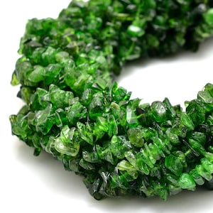 Puede incluir: Una hebra de chips de piedras preciosas verdes, probablemente peridoto, dispuestas en forma circular. Las virutas son irregulares en tamaño y forma, con un acabado brillante.