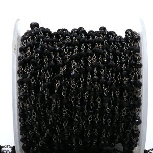 Op de afbeelding: Een spoel met zwarte edelsteen kralen en zilveren ketting, perfect voor het maken van sieraden.