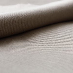 Puede incluir: Primer plano de una tela beige con textura acanalada. La tela est&aacute; doblada, creando una superficie suave y lisa.