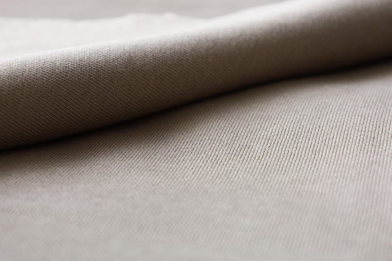 Puede incluir: Primer plano de una tela beige con textura acanalada. La tela est&aacute; doblada, creando una superficie suave y lisa.