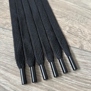 Könnte beinhalten: Ein Satz von acht schwarzen Schnürsenkeln mit schwarzen Metallösen. Die Schnürsenkel sind in einer Reihe angeordnet, wobei die Ösen zum Betrachter zeigen.