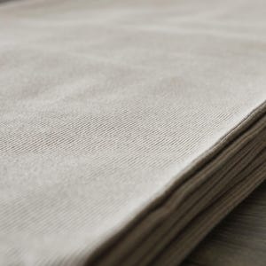 Puede incluir: Una pila de toallas de tela beige dobladas. Las toallas son suaves y texturizadas.