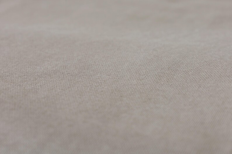 Puede incluir: Primer plano de una tela beige claro con una textura sutil. La tela tiene una superficie lisa y uniforme con un ligero brillo.