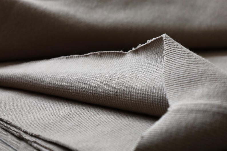Puede incluir: Primer plano de una tela suave de color beige con textura acanalada. La tela est&aacute; doblada por la mitad, creando una superficie lisa y uniforme.
