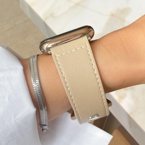 May include: A beige leather watch band is fastened on a wrist, paired with a silver bracelet. The watch has a silver case. The text "POLY BANDS" is visible at the bottom of the image.