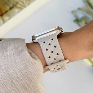 May include: A light grey braided watch band with a woven pattern. The band is made of a flexible material and has a silver buckle. The band is designed for a smartwatch.