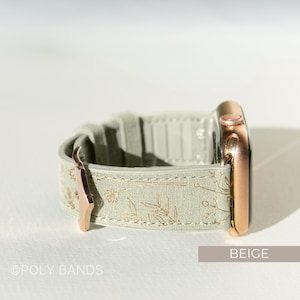 Op de afbeelding: Een beige Apple Watch band met een bloemenpatroon en ros&eacute;gouden hardware. De band is gemaakt van een zacht, getextureerd materiaal en heeft een klassieke uitstraling.