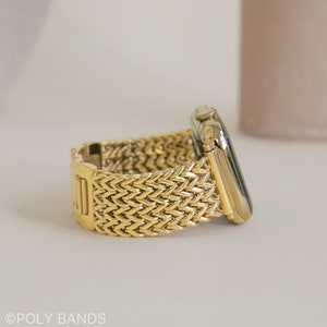 May include: A gold metal Apple Watch band with a woven herringbone pattern. The band is shown on a white surface.