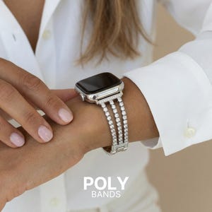 May include: A silver smartwatch with a sparkling, three-row diamond band is displayed. The watch is on a wrist, and the text "POLY BANDS" is at the bottom of the image. The person is wearing a white button-down shirt.