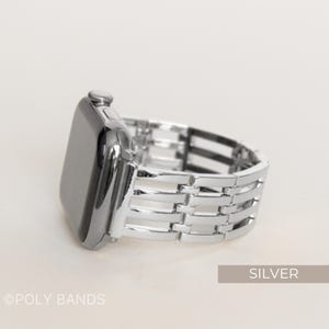 May include: Silver-colored watch band with a woven design. The watch face is black and shiny. The band is made of metal and has a polished finish. The word "SILVER" is in a rectangular box in the bottom right corner.