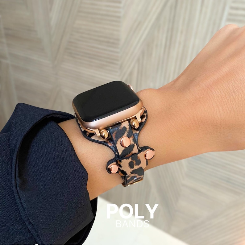 Puede incluir: Un Apple Watch de oro rosa con una banda de estampado de leopardo con tachuelas doradas. La banda est&aacute; hecha por POLY BANDS.