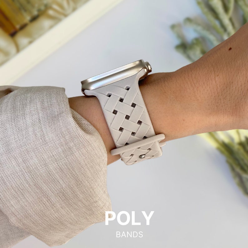 May include: A light grey braided watch band with a woven pattern. The band is made of a flexible material and has a silver buckle. The band is designed for a smartwatch.