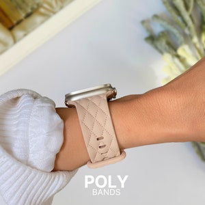 Puede incluir: Una banda de reloj Apple acolchada de color rosa claro con una hebilla plateada. La banda est&aacute; en la mu&ntilde;eca de una persona. El texto "POLY BANDS" est&aacute; en la parte inferior de la imagen.