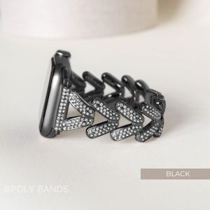 May include: Black watch band with a chevron design and clear rhinestones. The band is made of metal and has a polished finish.