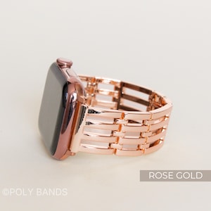 May include: Rose gold Apple Watch band with a woven design. The band is made of metal and has a shiny finish. The watch face is black. The text "ROSE GOLD" is in a white rectangle. The brand name "POLY BANDS" is at the bottom.