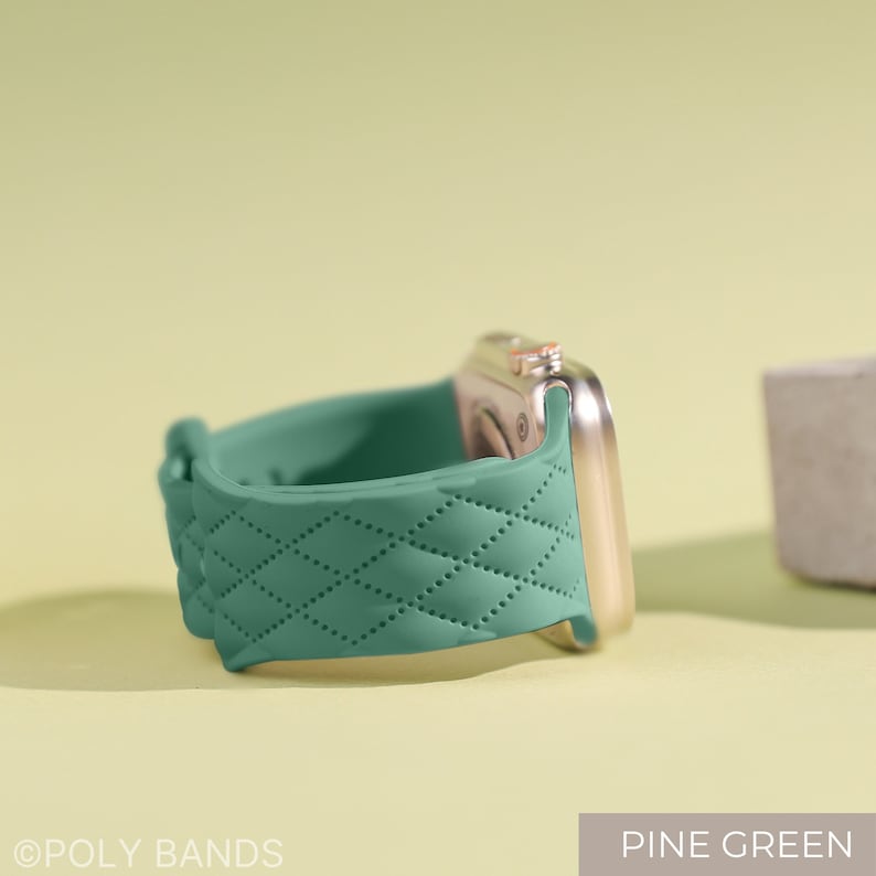 Puede incluir: Una correa de reloj de silicona verde acolchada para un Apple Watch. La correa tiene un patr&oacute;n de diamante y se muestra en un Apple Watch dorado.