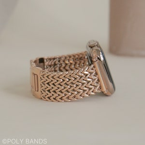 May include: A rose gold Apple Watch band with a woven, herringbone pattern.