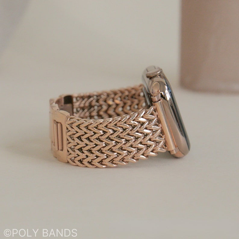 May include: A rose gold Apple Watch band with a woven, herringbone pattern.