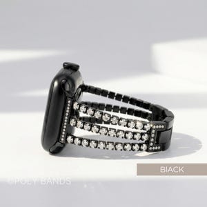 May include: Black Apple Watch with a three-row rhinestone band. The watch band is black with three rows of clear rhinestones. The watch is on a white surface. The text "BIACK" is in the bottom right corner, and "OPOLY BANDS" is in the bottom left corner.