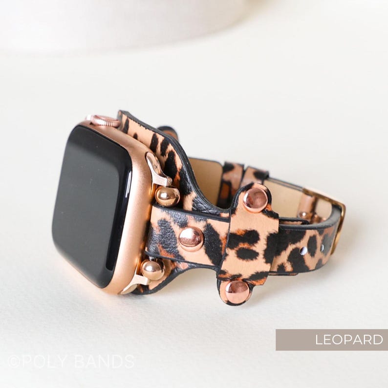 Puede incluir: Una correa de Apple Watch de oro rosa con un dise&ntilde;o de estampado de leopardo y tachuelas de oro rosa. La correa est&aacute; hecha de cuero y tiene un cierre de hebilla.