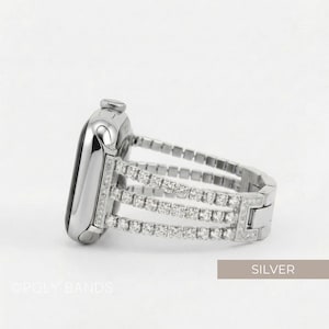 May include: Silver Apple Watch band with three rows of sparkling crystals. The band is made of silver-toned metal and features a secure clasp. The watch face is also silver and has a black screen. The word "SILVER" is in the image.