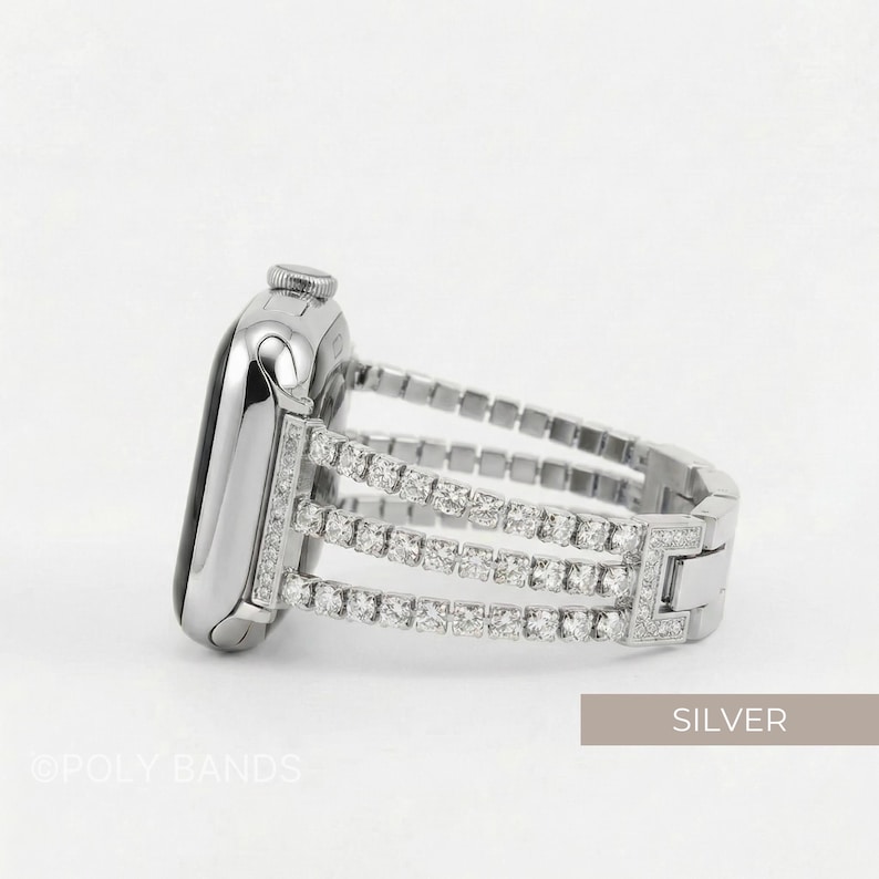 May include: Silver Apple Watch band with three rows of sparkling crystals. The band is made of silver-toned metal and features a secure clasp. The watch face is also silver and has a black screen. The word "SILVER" is in the image.
