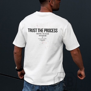 Puede incluir: Una camiseta blanca con el texto "TRUST THE PROCESS" y "ORIGINAL XD DESIGN" impreso en la espalda. La camiseta la lleva puesta una persona que lleva pantalones vaqueros azules y zapatillas blancas.