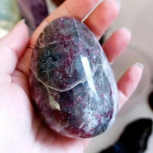 May include: A smooth, polished, egg-shaped red and grey gemstone with white veins and swirls.