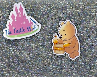 Puede incluir: Primer plano de una bolsa de cuentas de vidrio iridiscente. La bolsa tiene una pegatina con un castillo rosa y el texto "The Castle Wish". También hay una pegatina de Winnie the Pooh sosteniendo un tarro de miel.