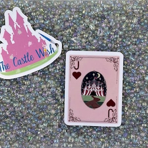 May include: A pink and white castle graphic with the text "The Castle Wish" on a white background. A pink playing card with a black jack of hearts symbol and a pink tent graphic with a night sky background.